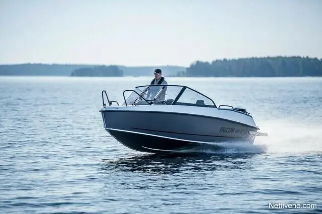 A man drives a Falcon boat on calm waters, surrounded by trees and distant shoreline, showcasing leisure boating activities.